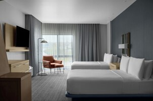 Habitación de hotel moderna con dos camas, un escritorio, una silla y un televisor.