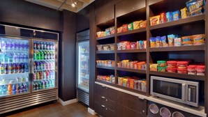 A self-service snack and beverage area with refrigerated drink dispensers and shelves stocked with snacks and packaged foods. - Courtyard Lehi at Thanksgiving Point (Lehi)