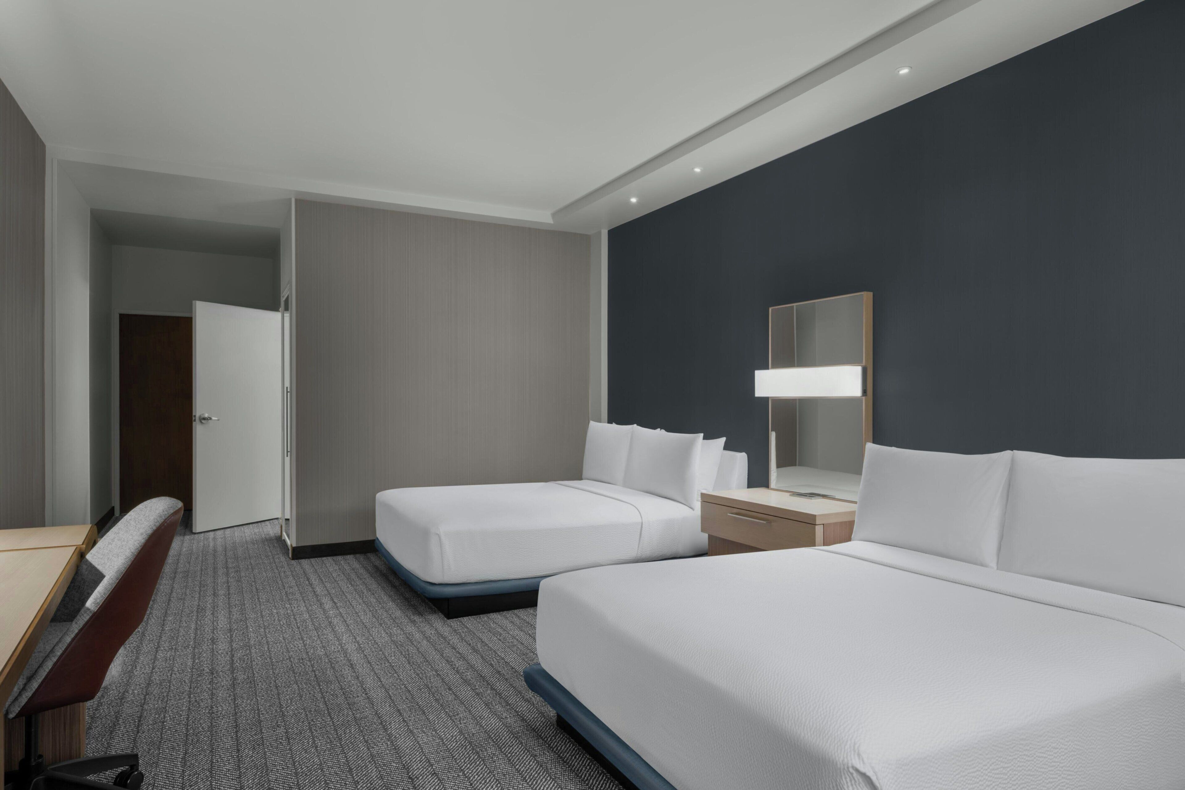 Habitación de hotel con dos camas, un escritorio, una silla, un armario y un espejo.