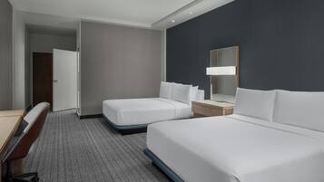 Habitación de hotel con dos camas, un escritorio, una silla, un armario y un espejo.
