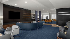 A modern hotel lobby with a curved seating area, a flat-screen TV, and a dining area with yellow chairs. - Courtyard Lehi at Thanksgiving Point (Lehi)