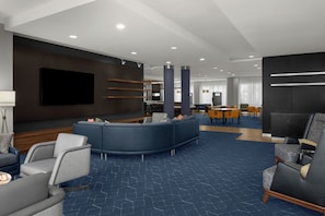 A modern hotel lobby with a curved seating area, a flat-screen TV, and a dining area with yellow chairs. - Courtyard Lehi at Thanksgiving Point (Lehi)