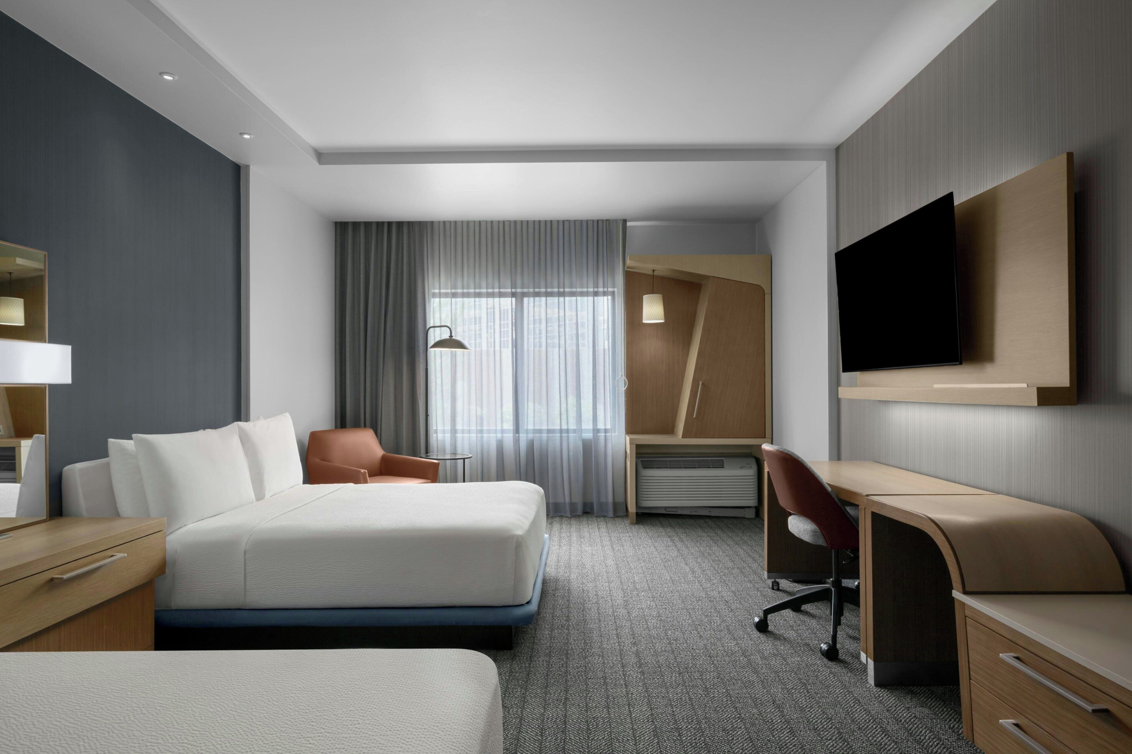 A hotel room with a bed, a desk, a chair, a television, and a window with curtains.