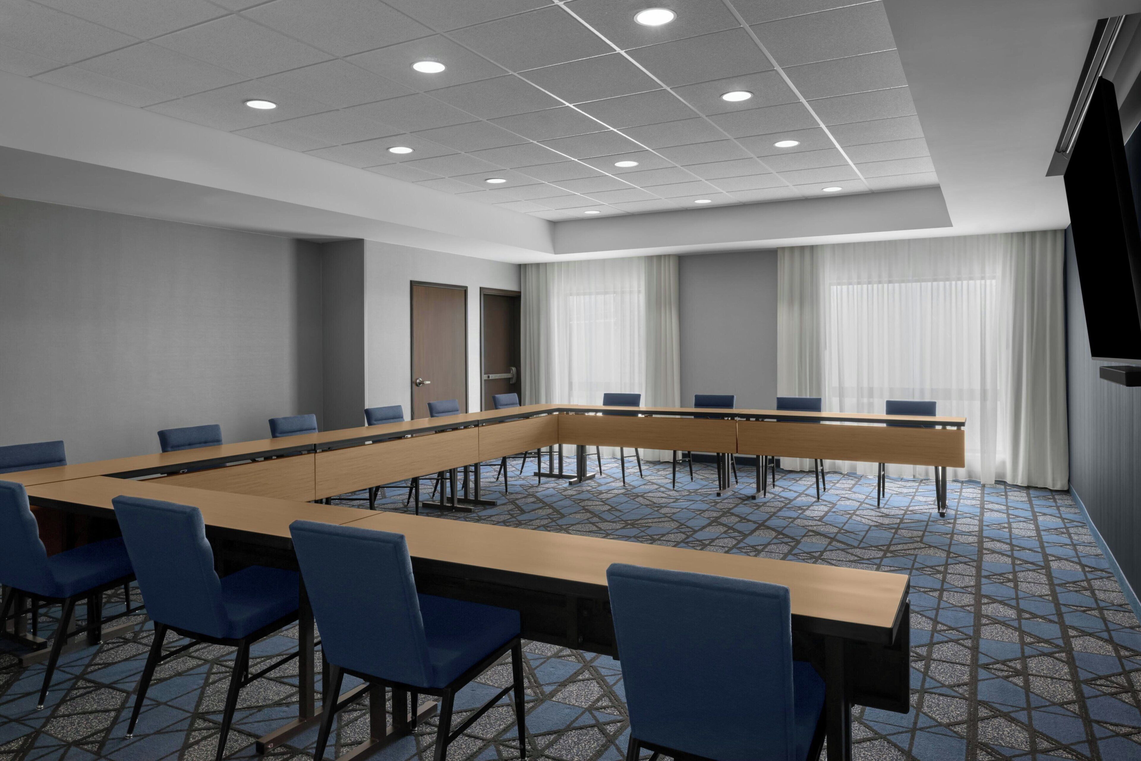 A conference room with a long table, blue chairs, a door, and a large window with curtains.