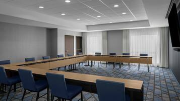 A conference room with a long table, blue chairs, a door, and a large window with curtains.