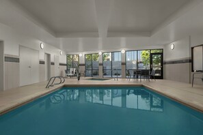 A swimming pool with a tiled deck, a sun terrace with chairs, and large windows offering a view of the outdoors. - Courtyard Lehi at Thanksgiving Point (Lehi)