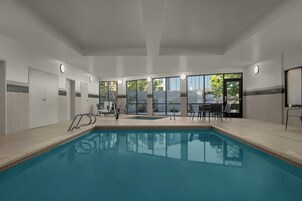 Una piscina con solárium empedrado, una terraza con sillas y amplias ventanas con vistas al exterior.