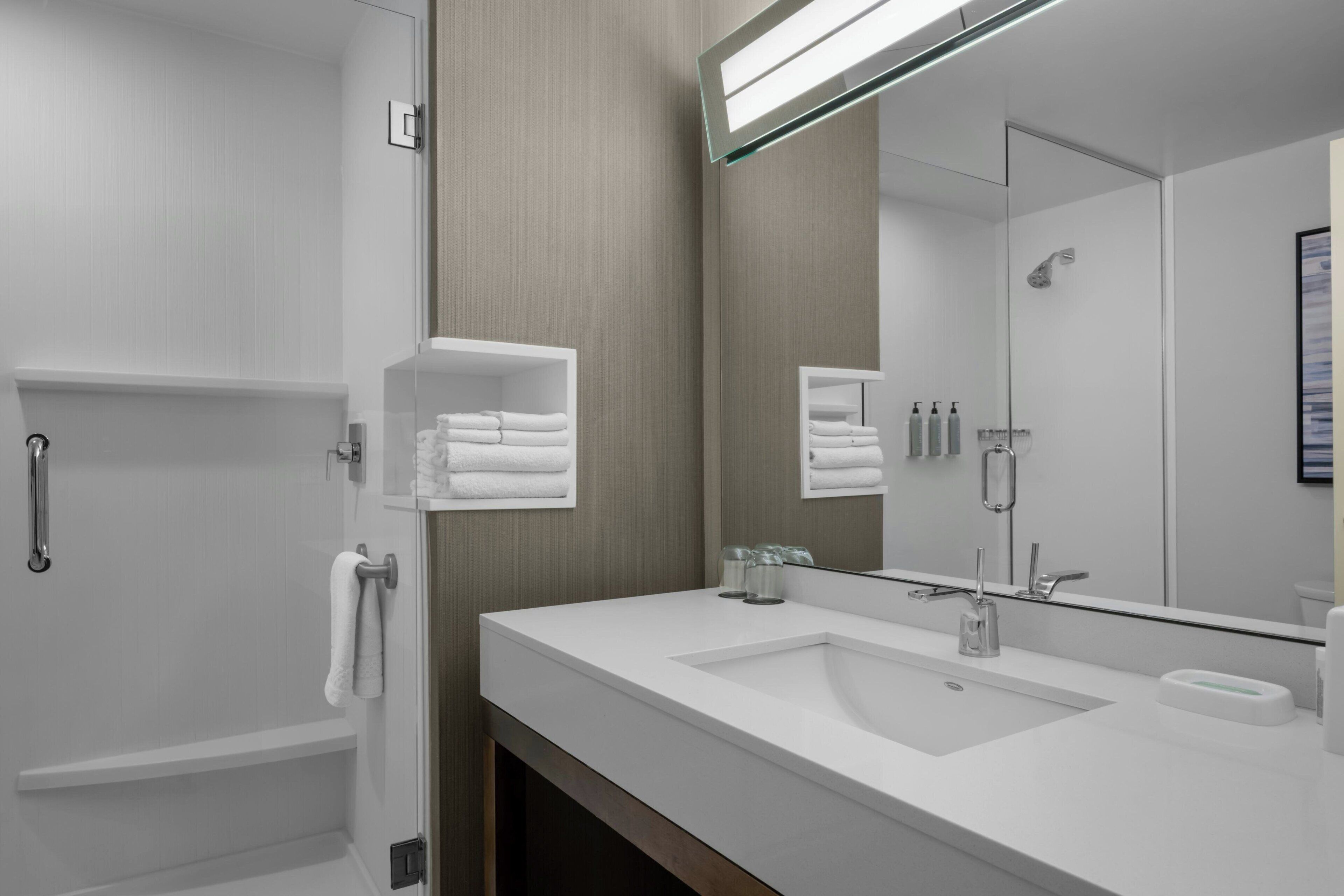 Un baño moderno con un espejo grande, un lavabo y una ducha.