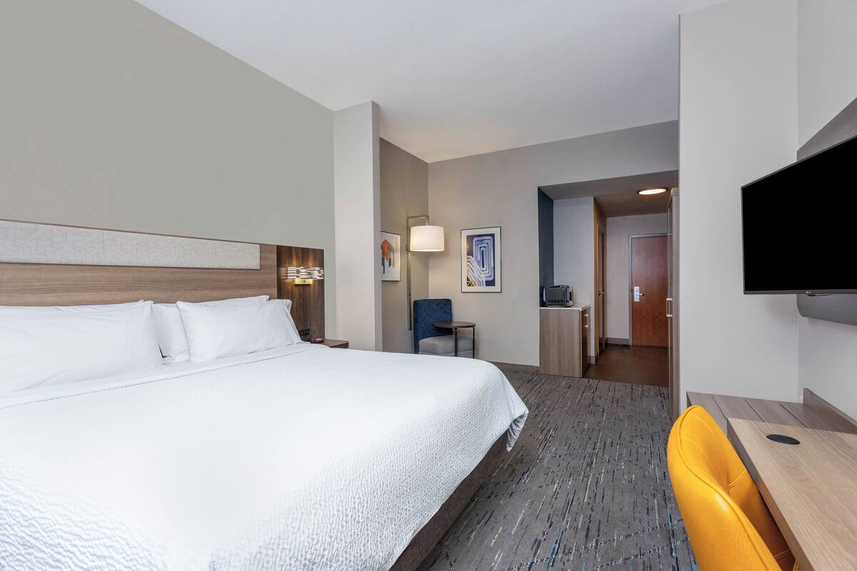 A hotel room with a large bed, a desk, a chair, and a flat-screen TV.
