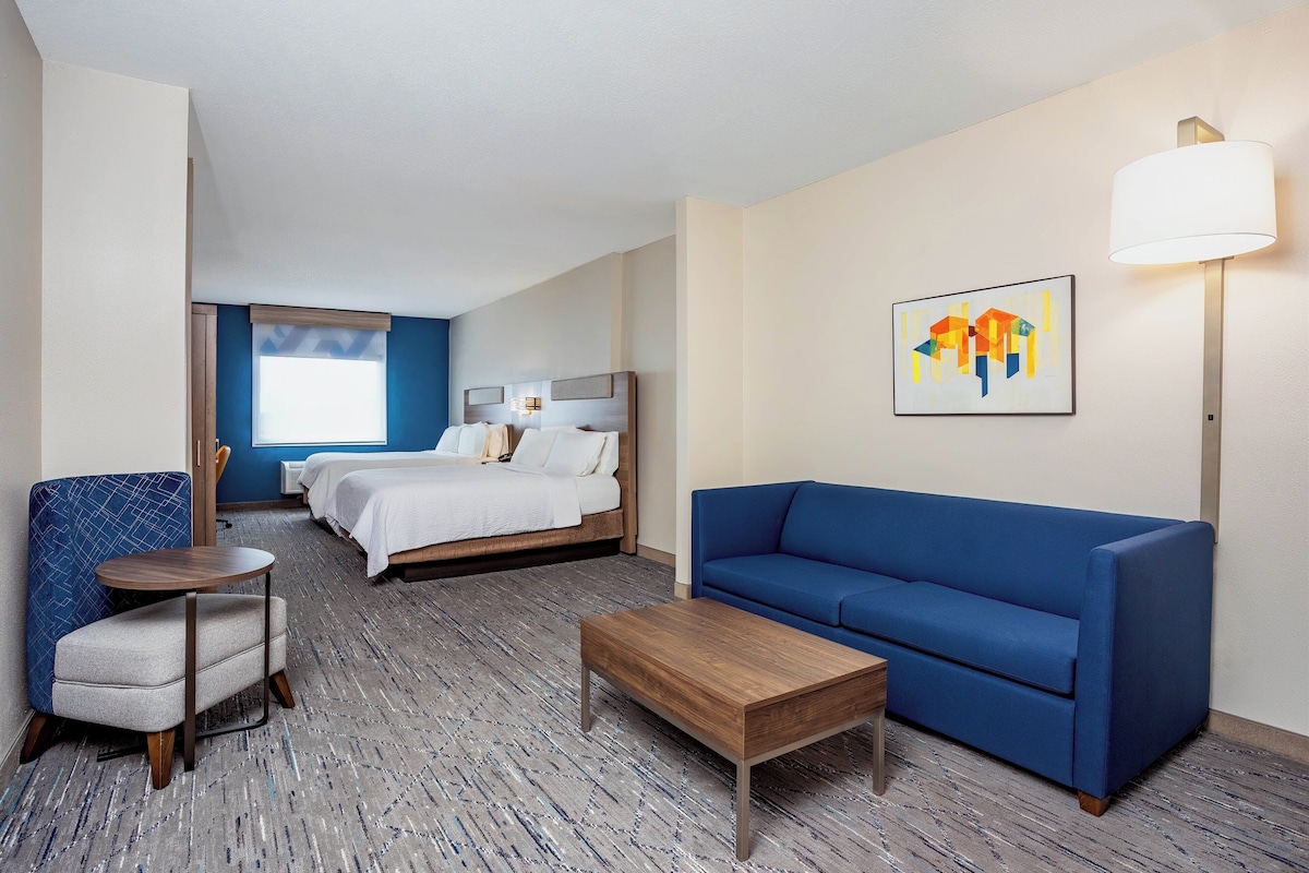 A hotel room with a bed, a blue sofa, a small table, and a chair.