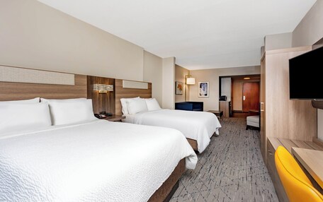 A hotel room with two beds, a TV, a desk, and a bathroom visible in the background.