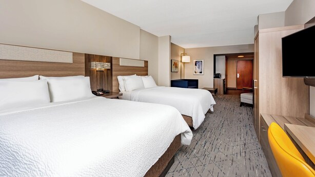 A hotel room with two beds, a TV, a desk, and a bathroom visible in the background.