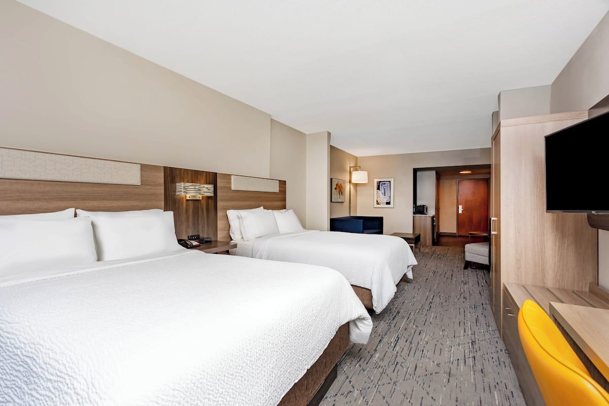 A hotel room with two beds, a TV, a desk, and a bathroom visible in the background.