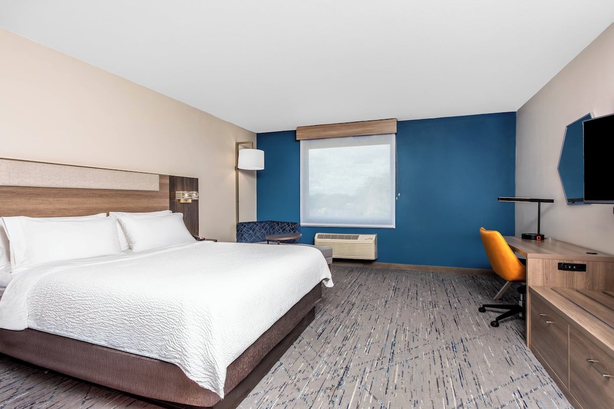 A hotel room with a large bed, a desk with a chair, a television, and a window with a view.