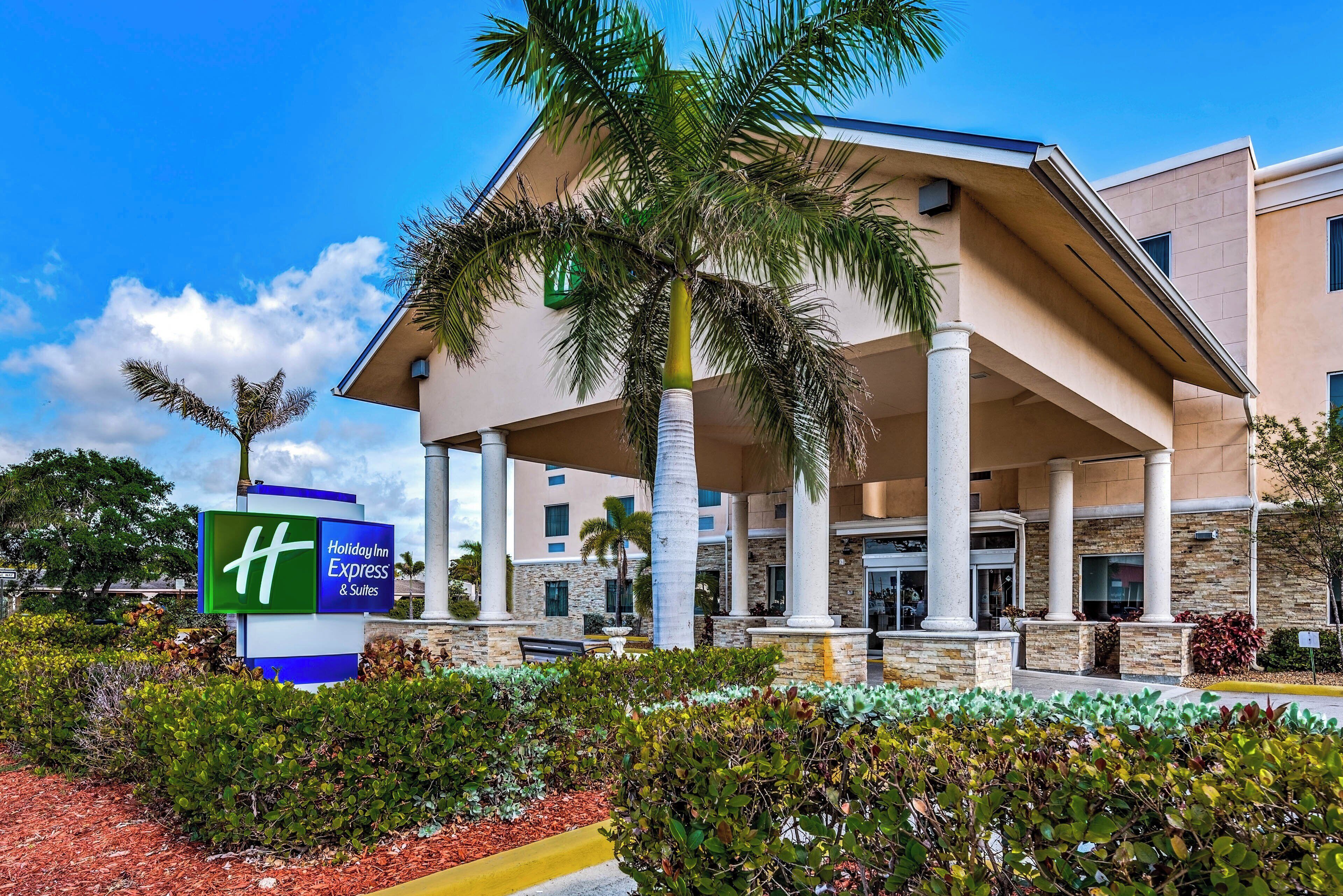 Un hôtel Holiday Inn Express & Suites doté d’une entrée couverte, de palmiers et d’un jardin aménagé.