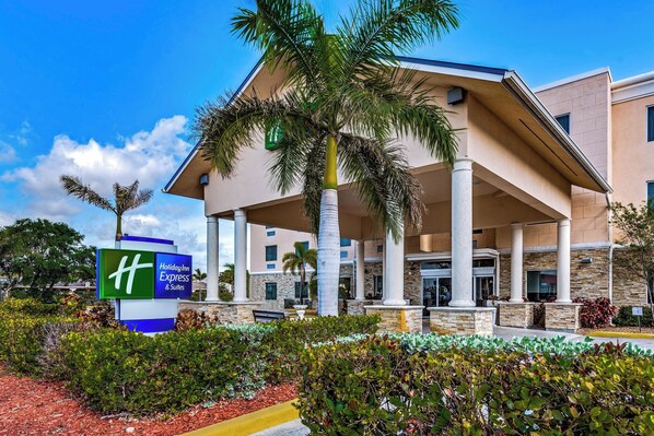 Un Holiday Inn Express & Suites con entrada cubierta, palmeras y un jardín ajardinado.