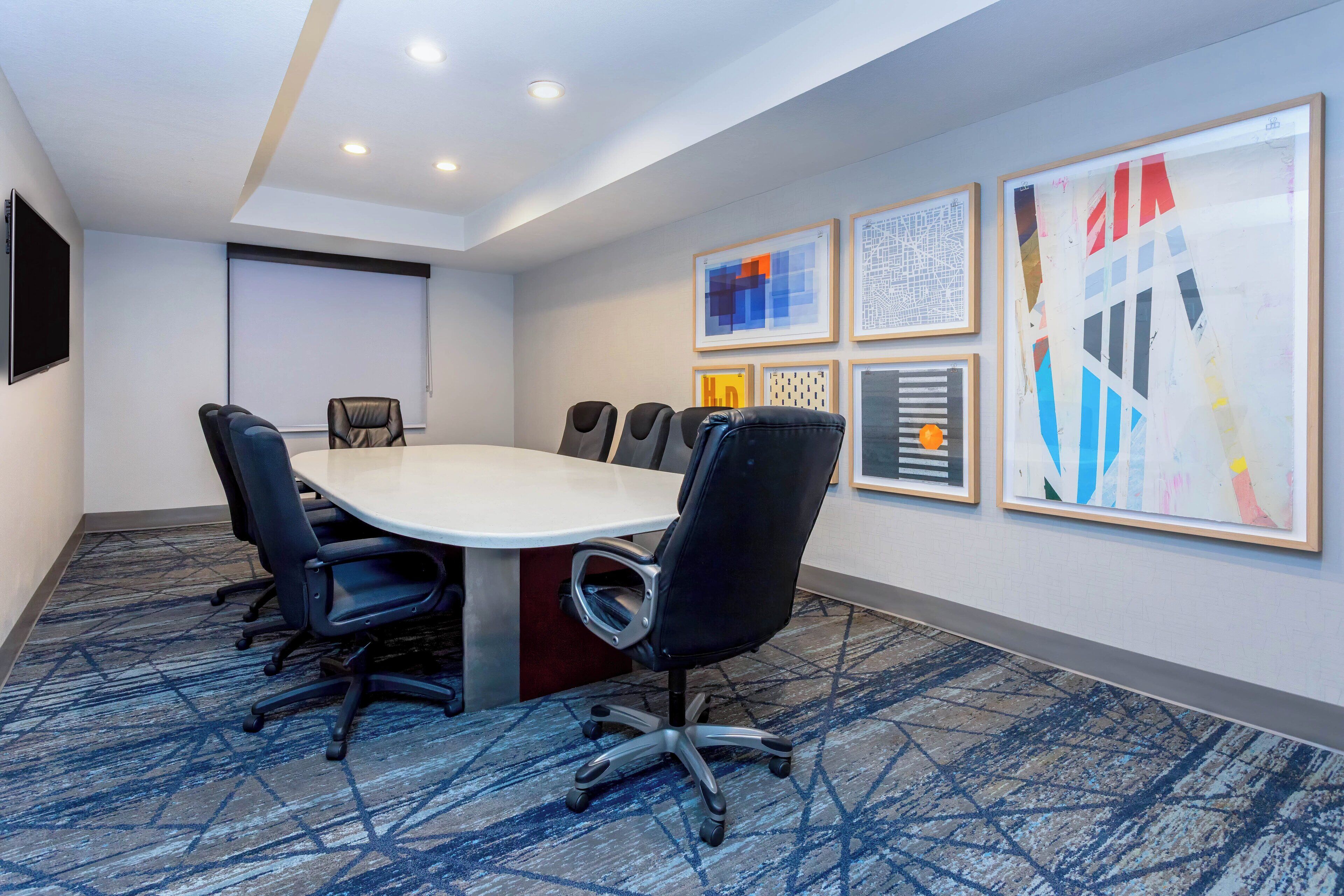A conference room with a large oval table, six black office chairs, and a carpeted floor.