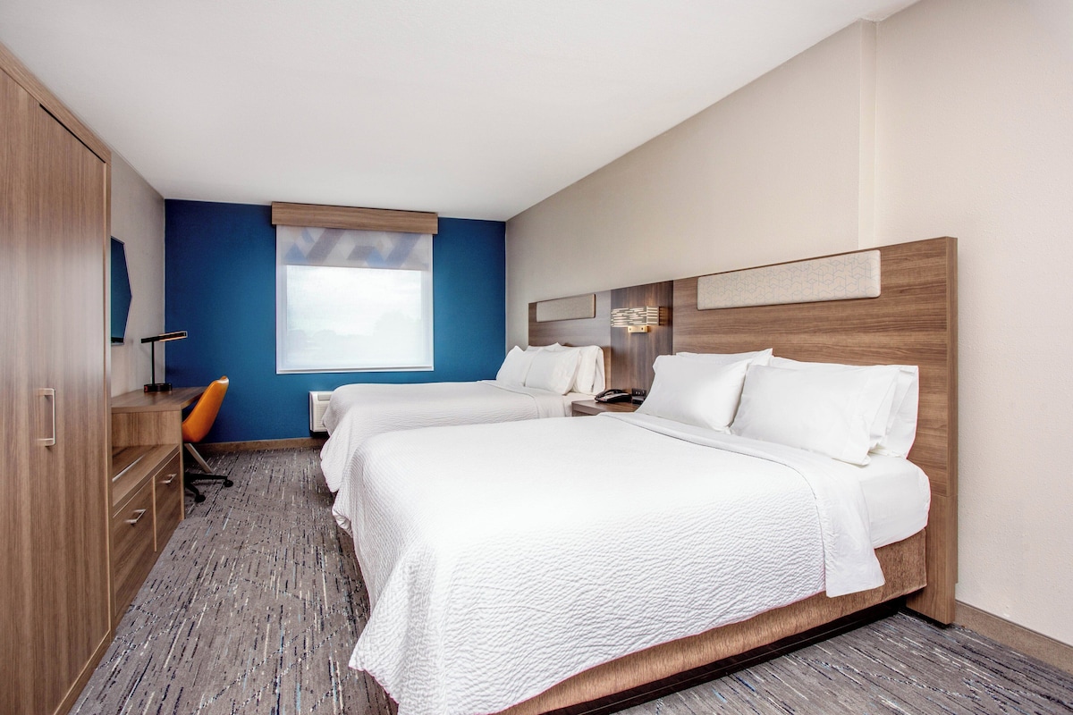 A hotel room with two beds, a desk, and a chair.