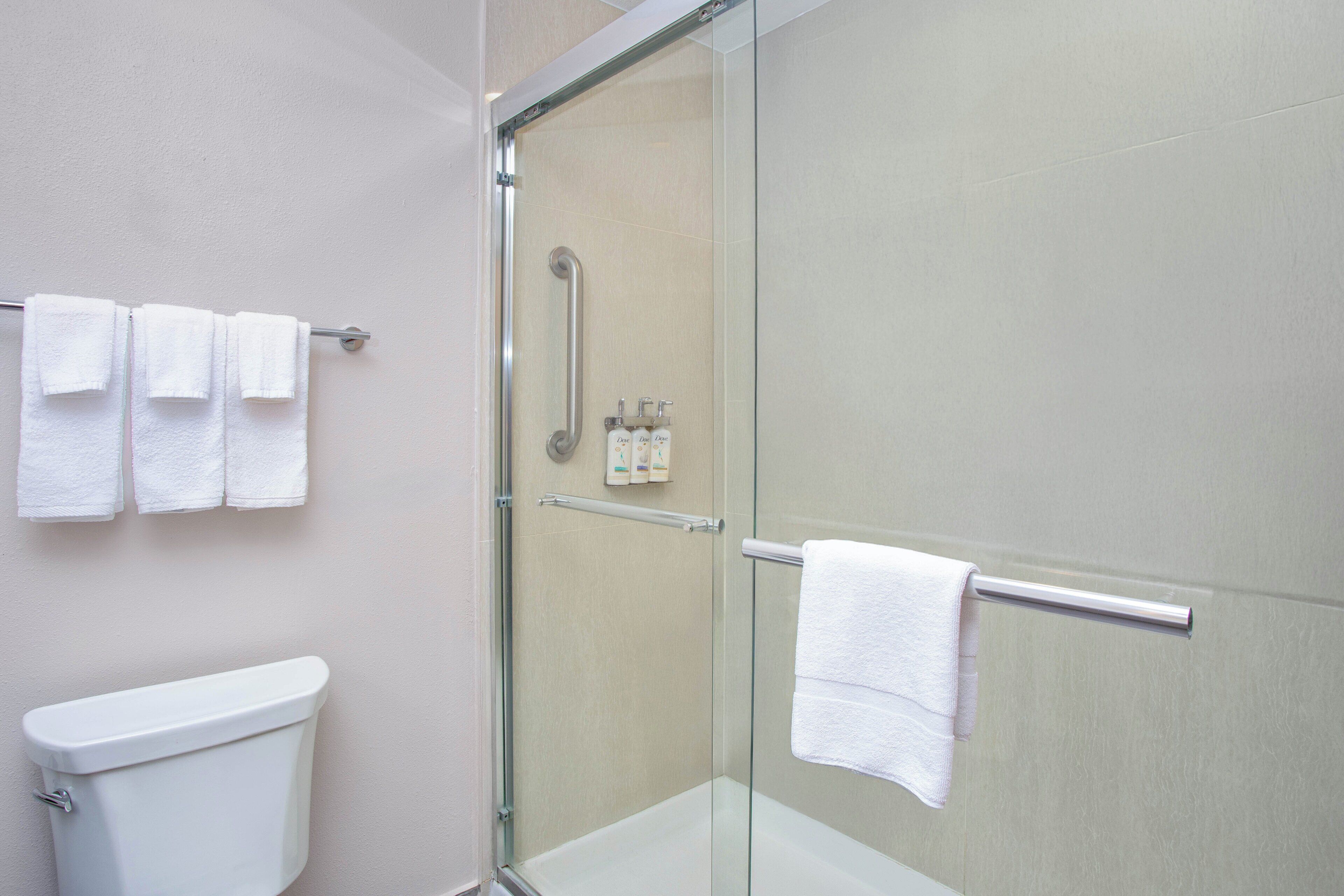 A bathroom with a glass shower enclosure, a toilet, and a towel rack with multiple white towels.