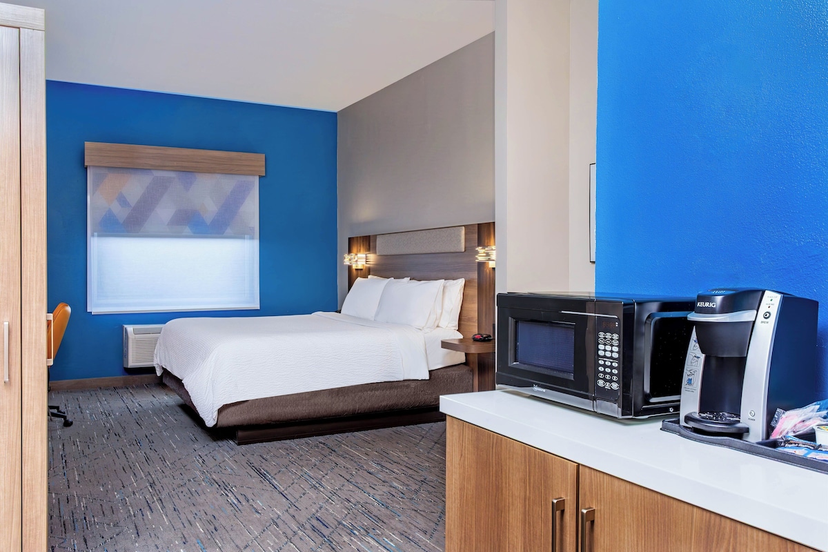A hotel room with a bed, a minibar, a microwave, and a coffee maker.