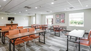 A conference room with multiple tables and chairs, large windows, and a flat-screen TV on the wall.