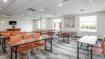 Une salle de conférence équipée de plusieurs tables et chaises, de grandes fenêtres et d’un téléviseur à écran plat fixé au mur.