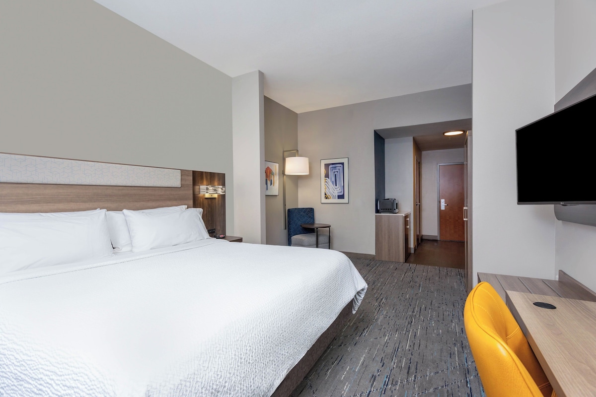 A hotel room with a large bed, a desk, a chair, and a flat-screen TV.