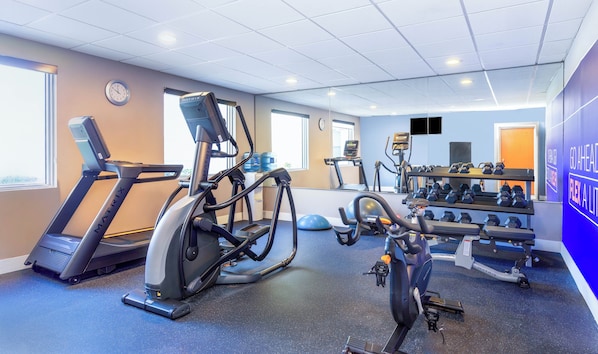 Een sportschool met loopbanden, een elliptische trainer, een roeimachine en een dumbbellsrek.