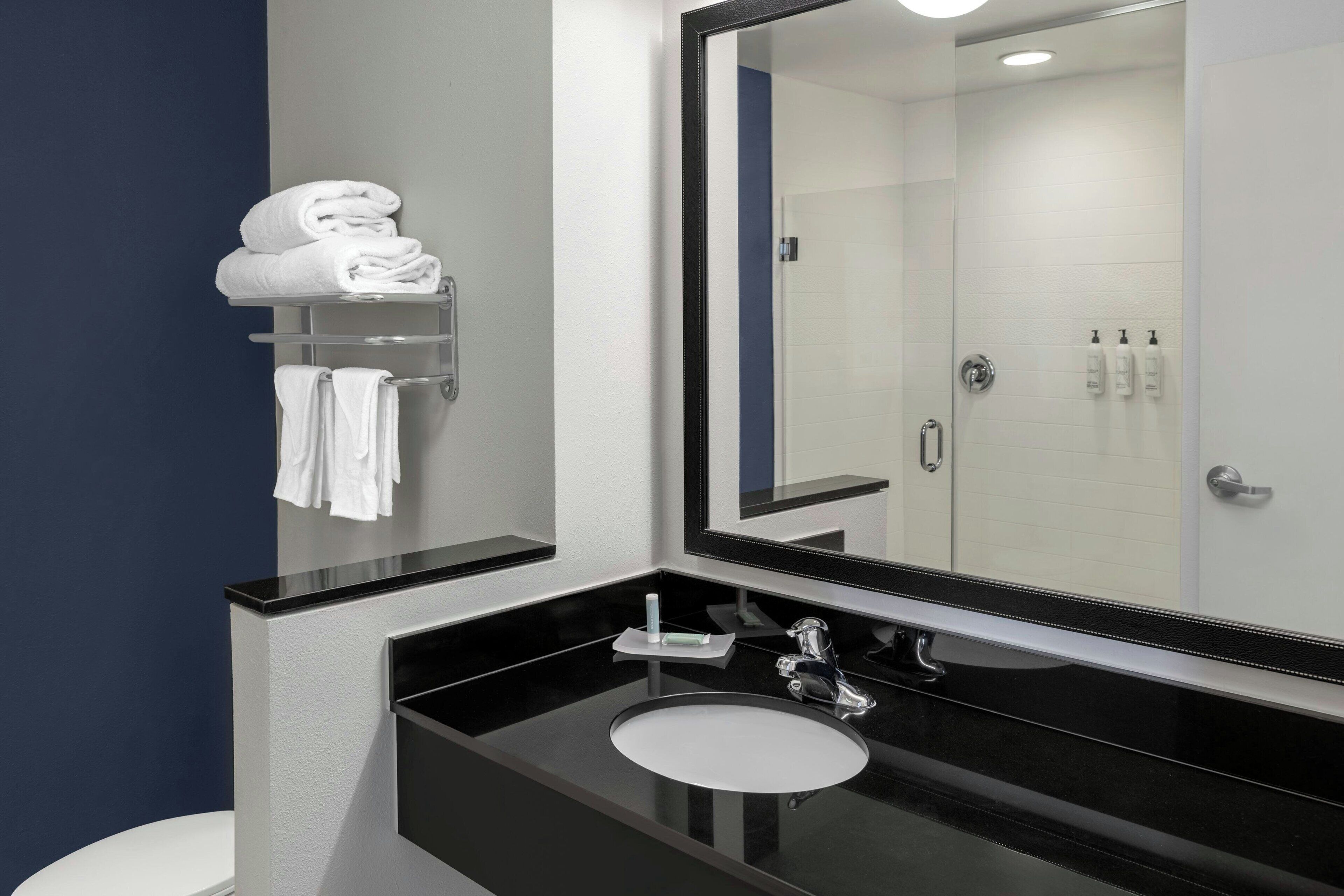 Un baño moderno con encimera negra, lavabo blanco y un espejo grande.