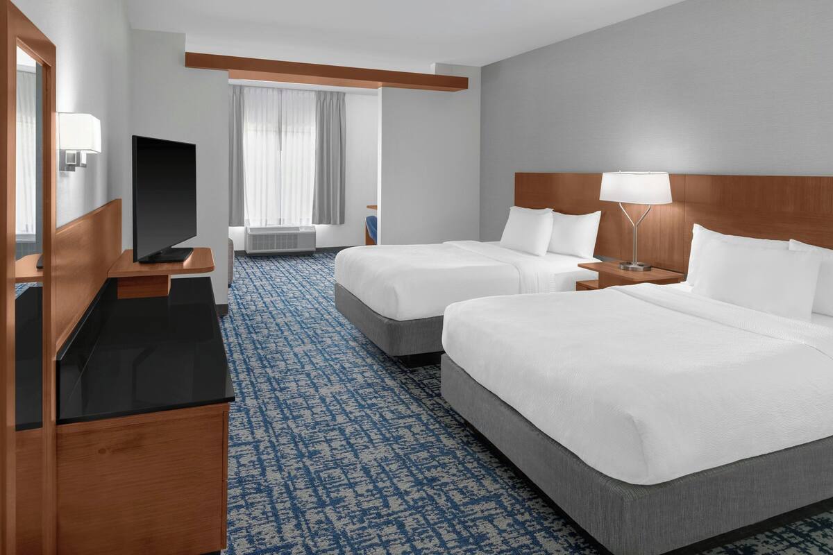A hotel room with two beds, a TV, a desk, and a window with curtains.
