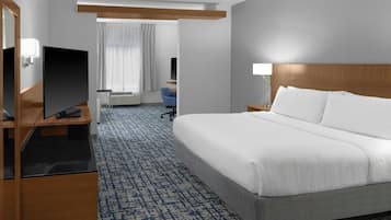 Habitación de hotel con una cama grande, un escritorio con televisor de pantalla plana, una silla y una ventana con cortinas.