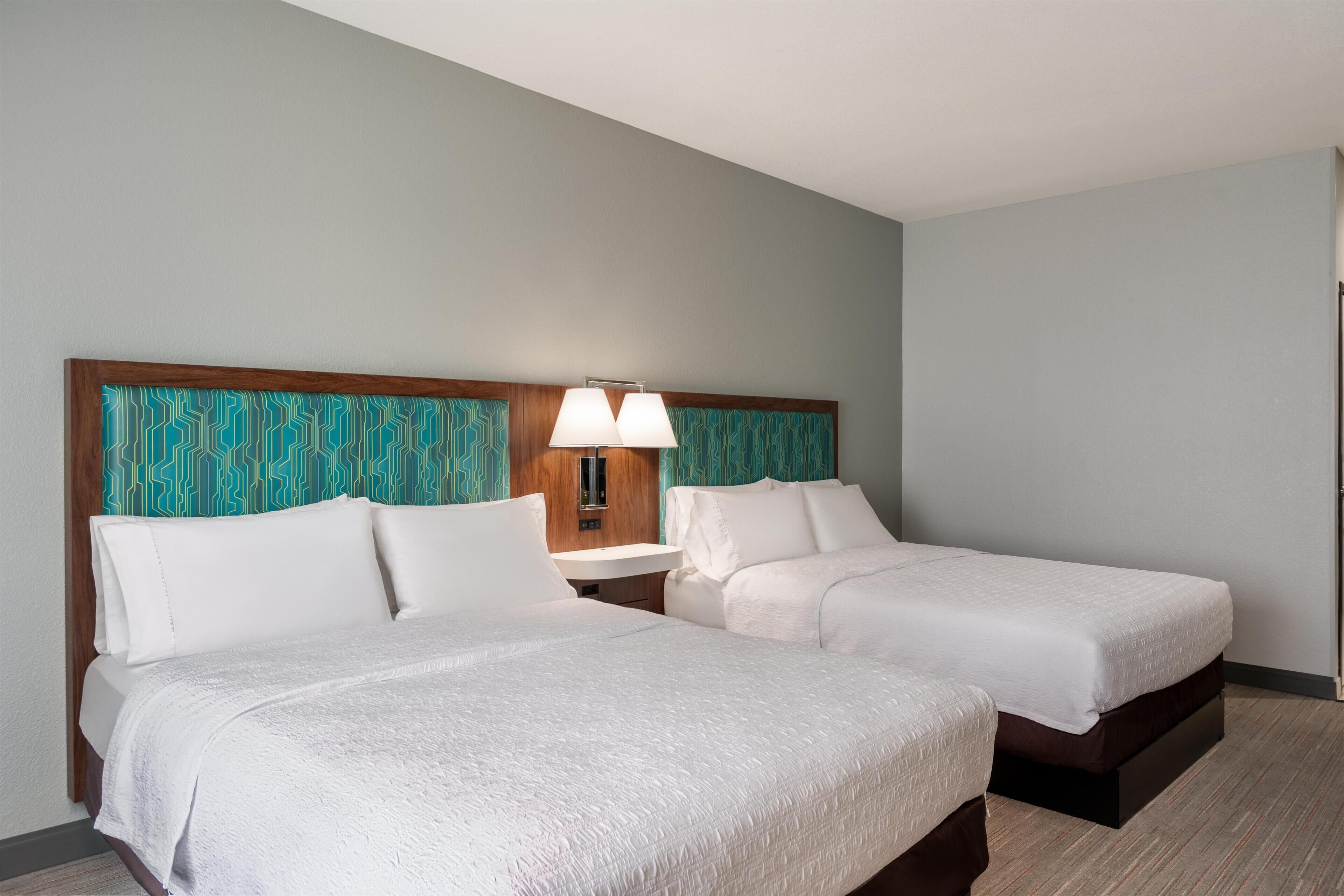 Una habitación de hotel con dos camas, una mesita de noche y una lámpara fijada a la pared.