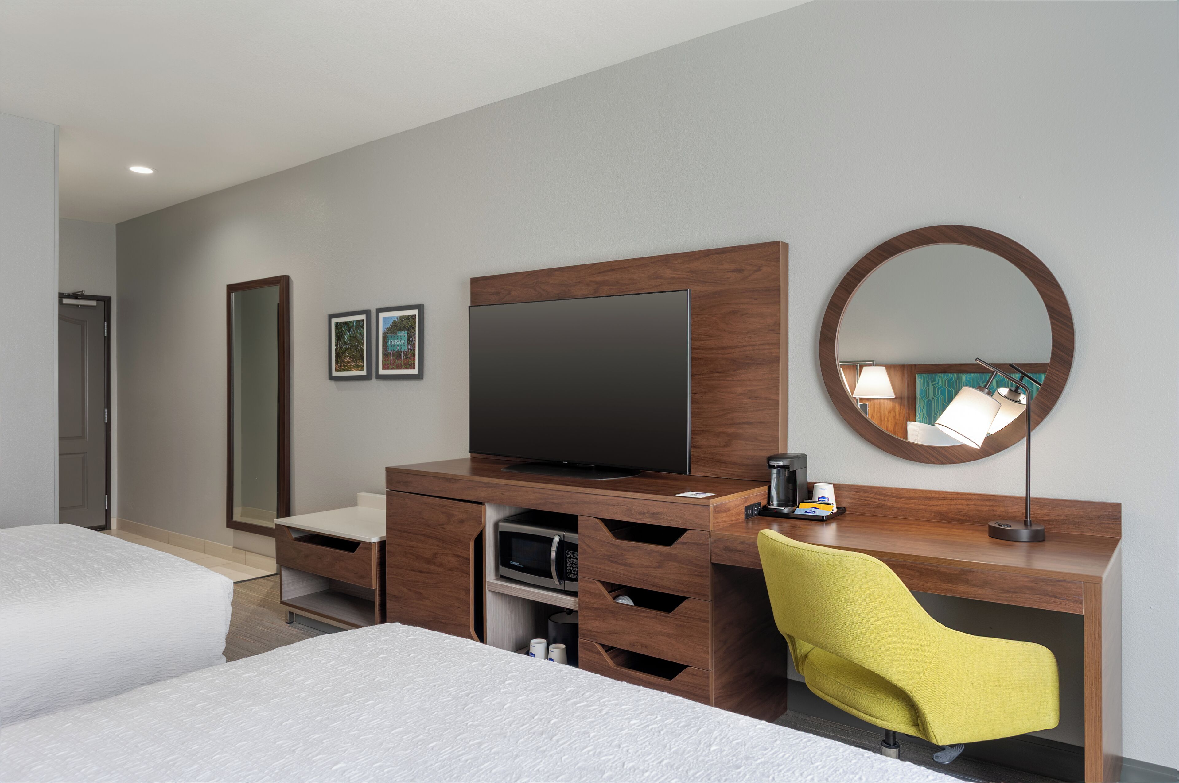 Une chambre d’hôtel avec deux lits, un bureau en bois équipé d’un téléviseur à écran plat, un four à micro-ondes, une machine à café et une chaise jaune.