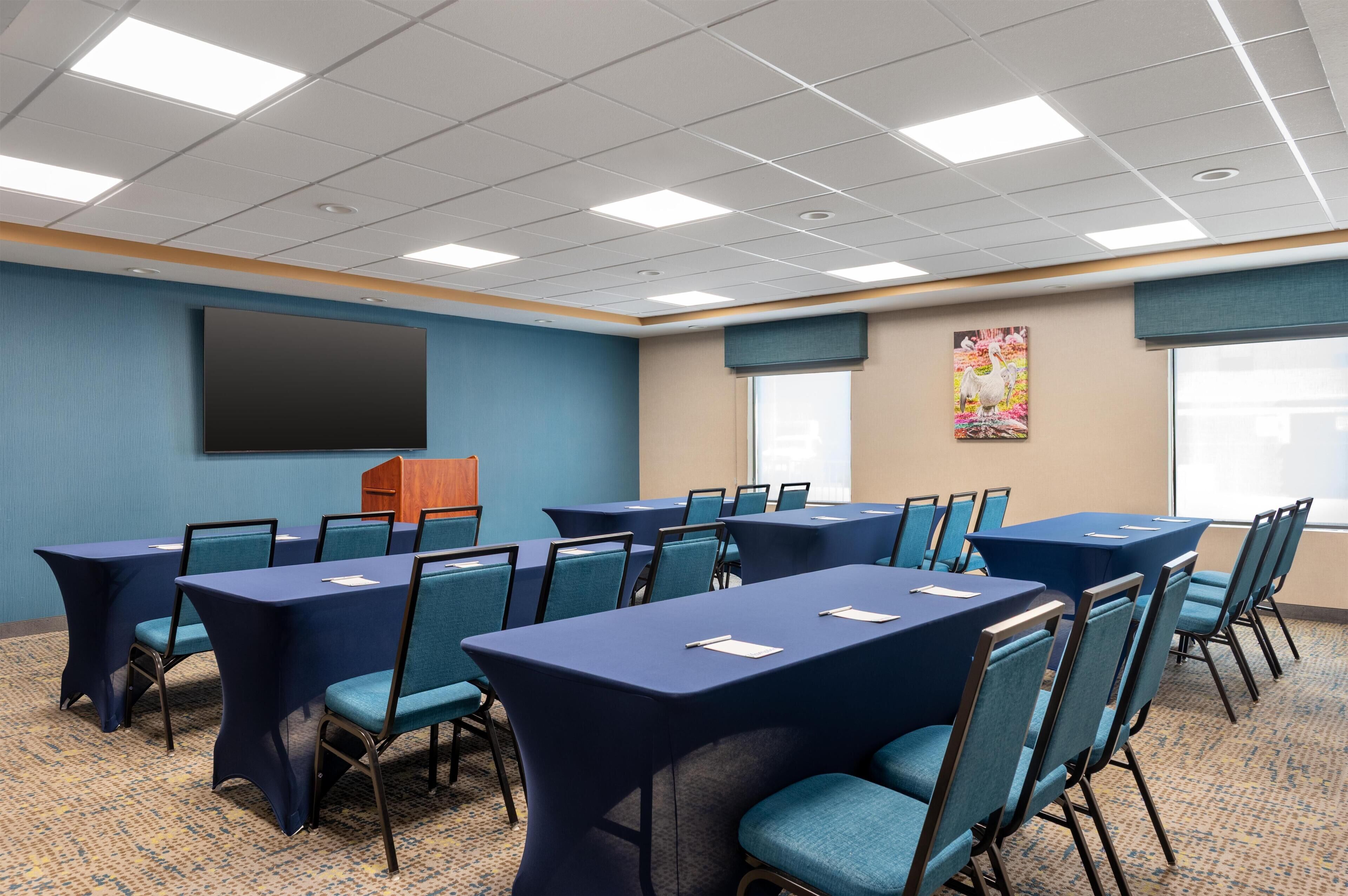 Un salón de conferencias con mesas y sillas, una pantalla grande y un ventanal con vistas.
