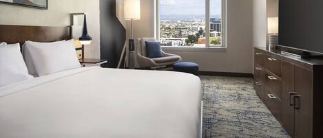 Une chambre d’hôtel avec un grand lit, une chaise, une télévision et une fenêtre donnant sur la ville.