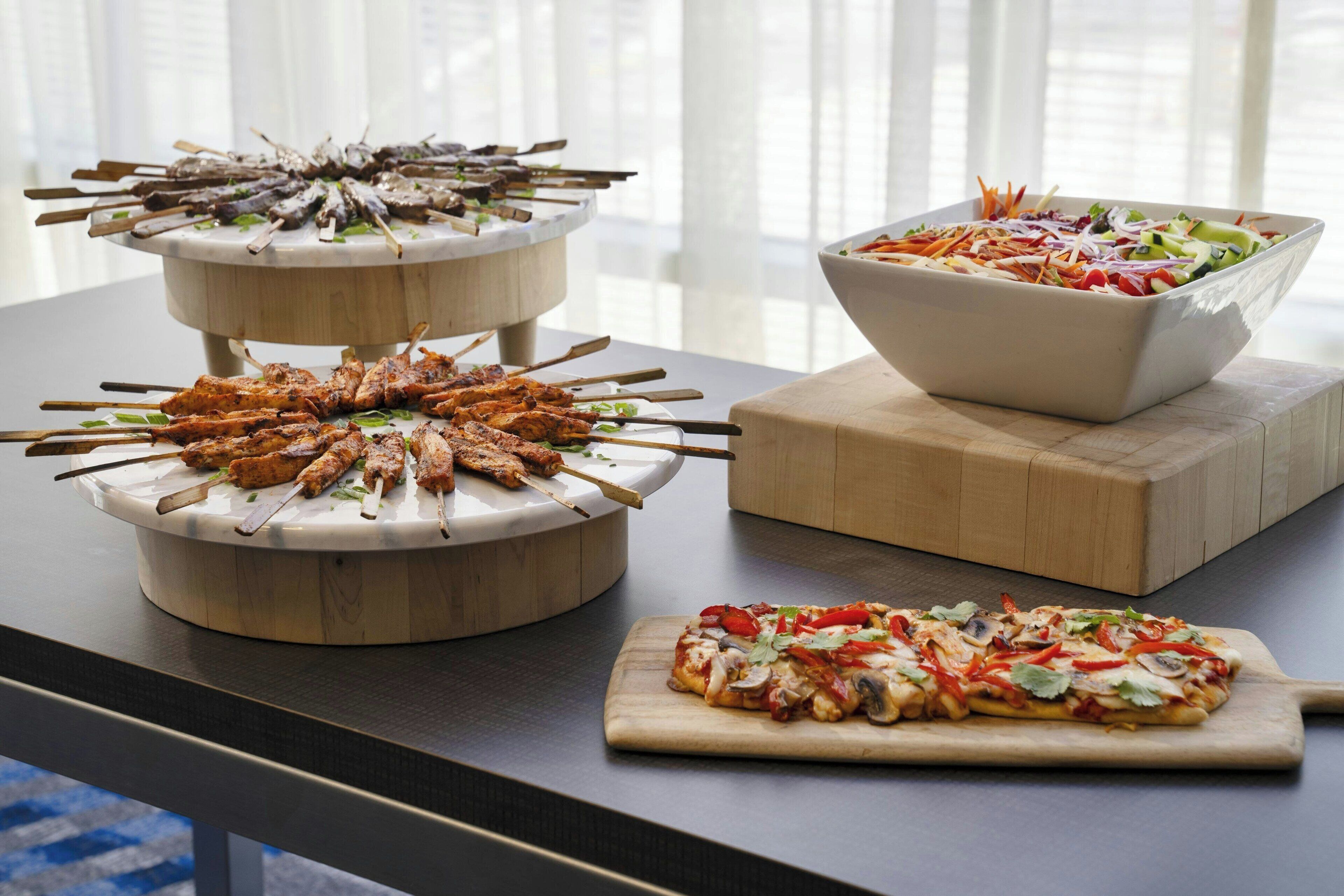 Une table de buffet avec des brochettes, une salade et une pizza.