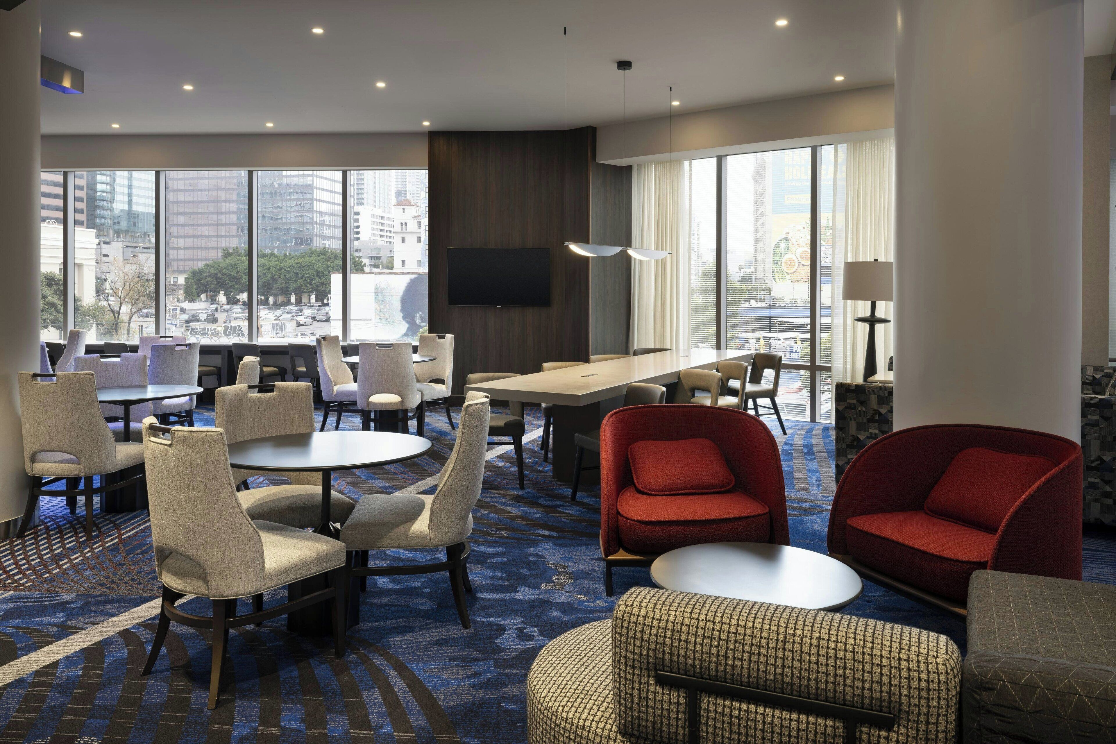 A hotel lobby with a mix of seating options, including chairs and sofas, a large table, and a television mounted on the wall.