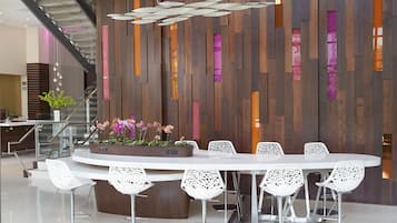 A modern dining area with a round table and white chairs, a wooden accent wall, and a staircase in the background.