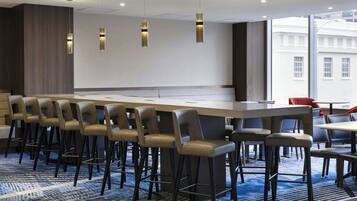 En modern hotellobby med en lång bardisk, flera olika sittgrupper och stora fönster med utsikt över staden.