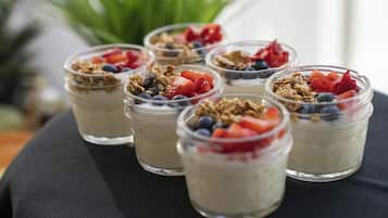A row of clear glass jars containing yogurt topped with granola and fresh fruits like strawberries and blueberries.