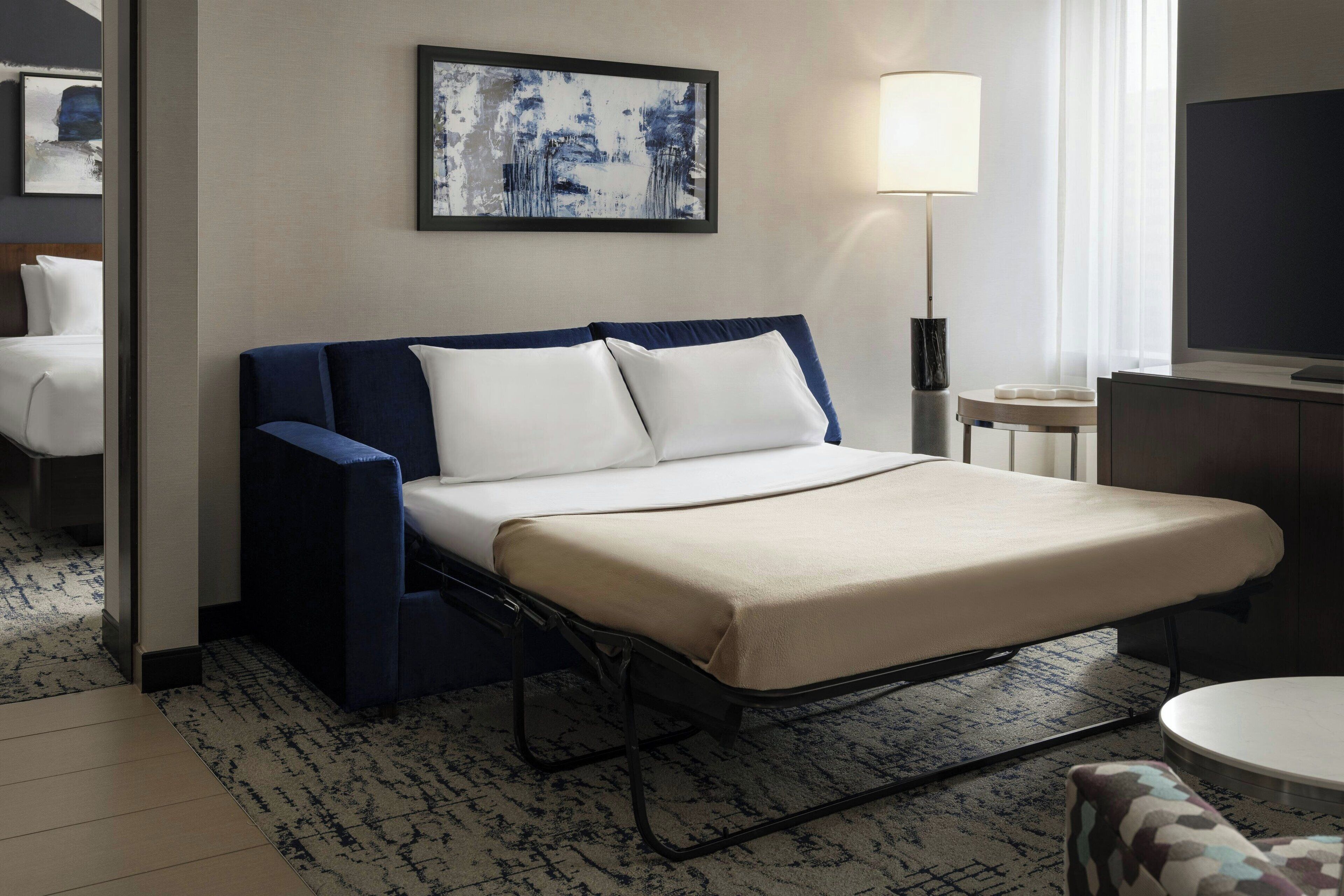 A hotel room with a bed, a bedside lamp, a television, and a painting on the wall.