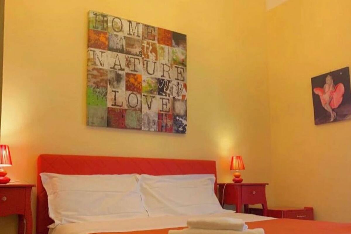 A hotel room with a bed, two bedside tables, a wall art piece, and a framed picture.