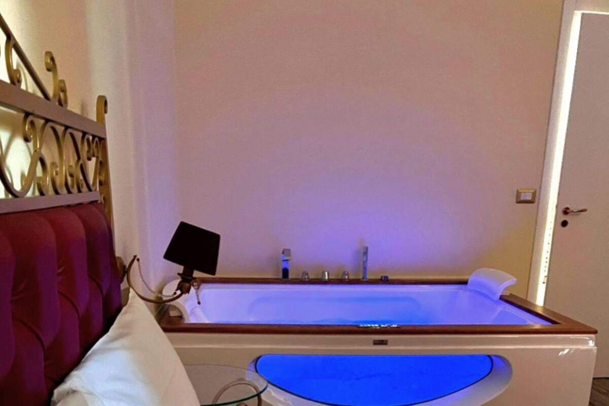 A room with a bed, a large bathtub, and a red headboard.