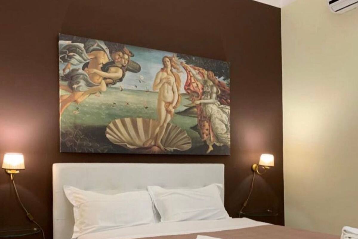A neatly made bed with a brown blanket, white pillows, and a white headboard. There are two wall-mounted lamps on either side of the bed.