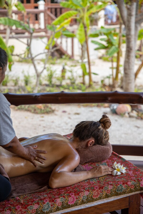 A person receiving a massage on a bench outdoors with a floral tablecloth, surrounded by greenery.