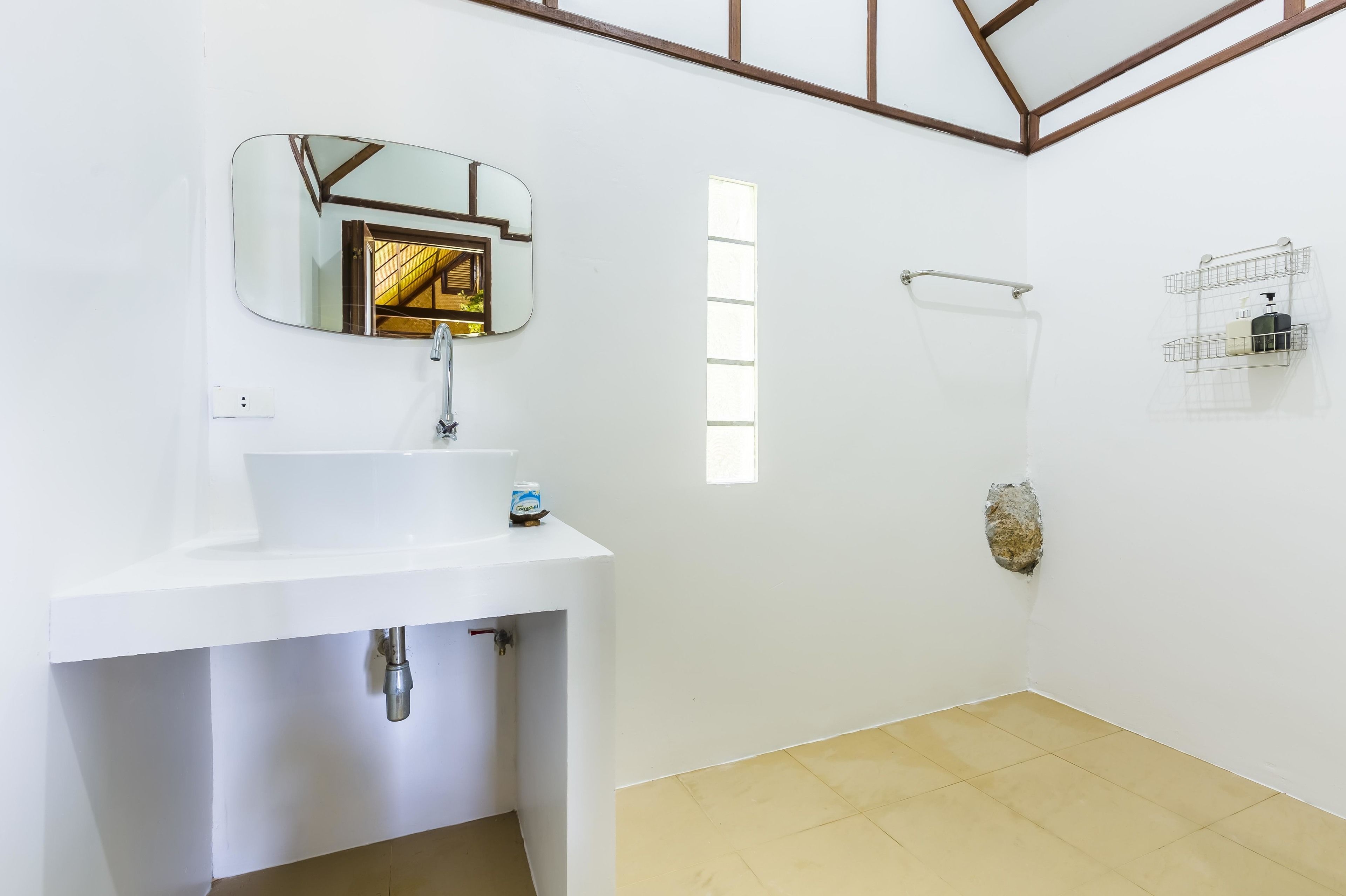 Un baño con lavamanos blanco, un espejo, zona de ducha y una ventana.