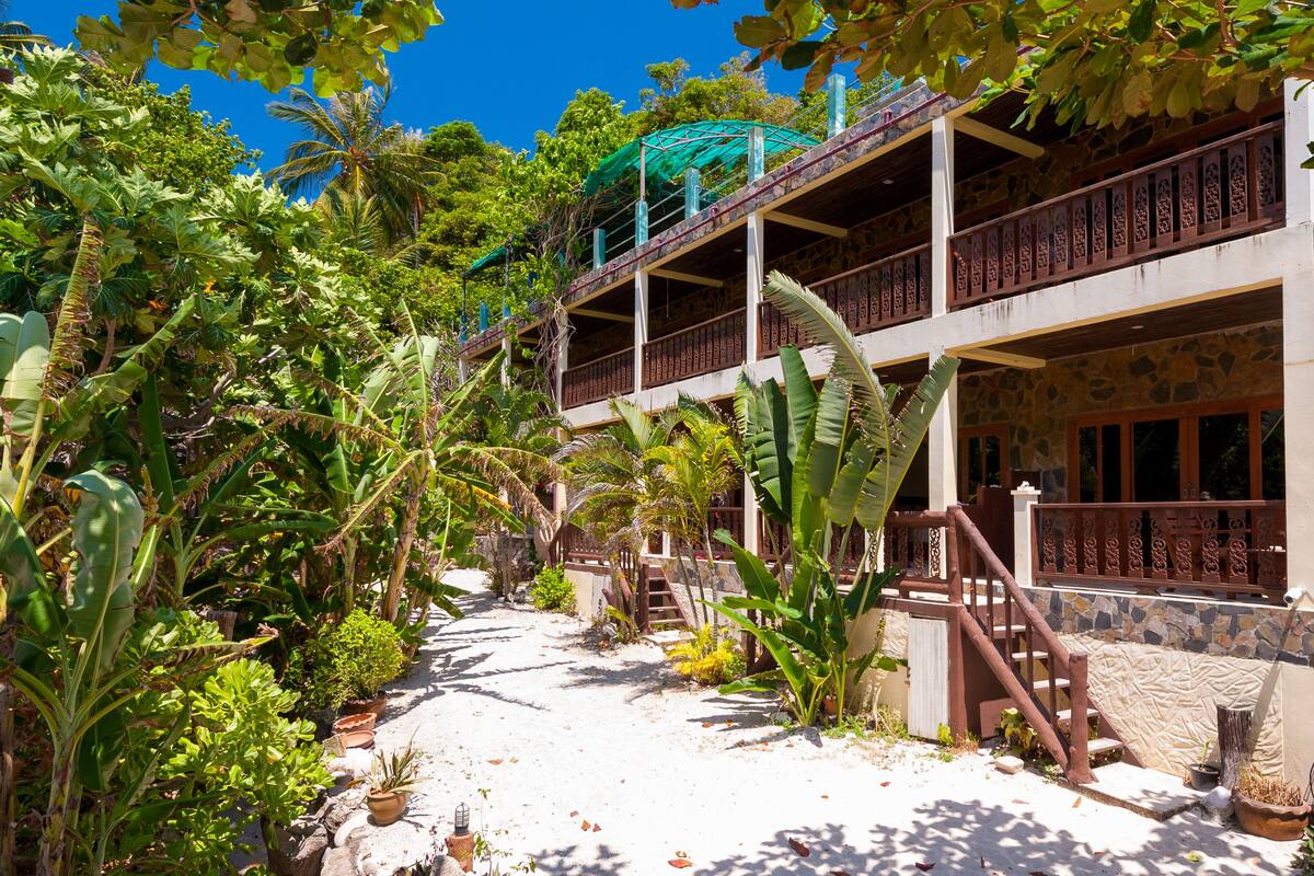 A multi-story building with balconies, surrounded by lush tropical vegetation.