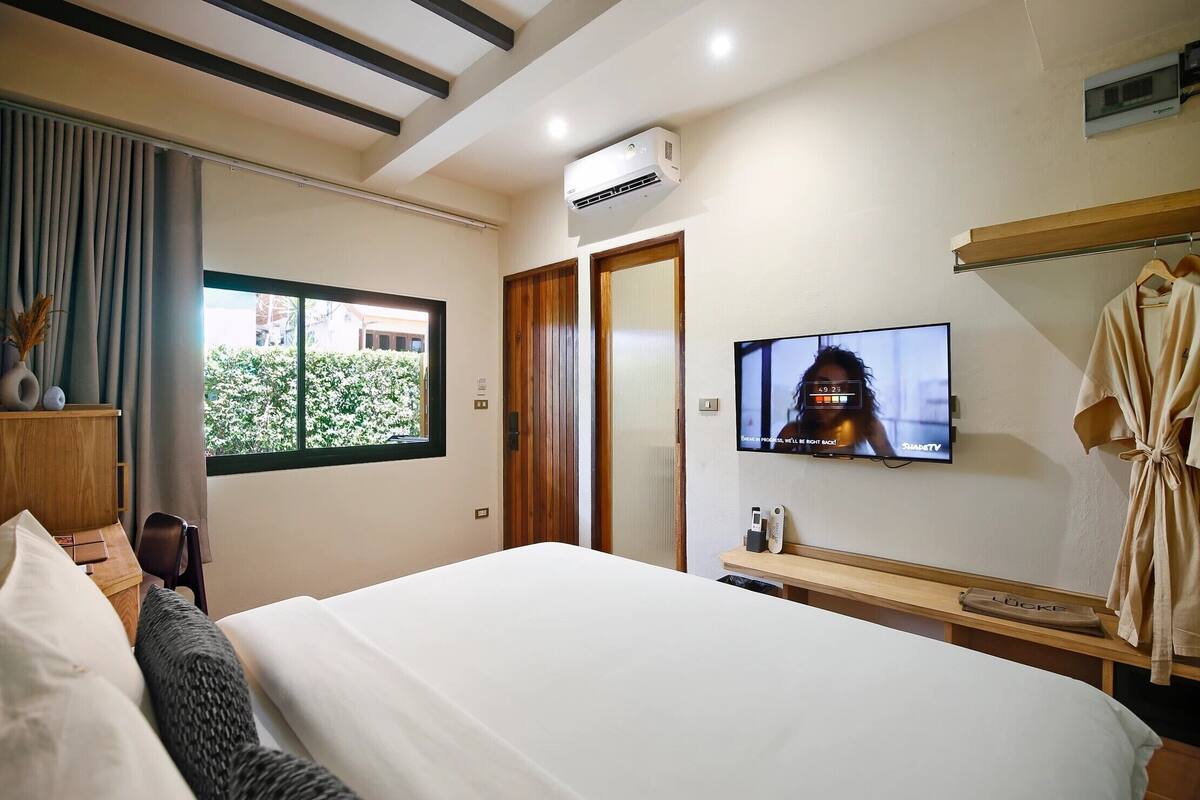 Een hotelkamer met een bed, een televisie, een kledingroede en een raam met gordijnen.