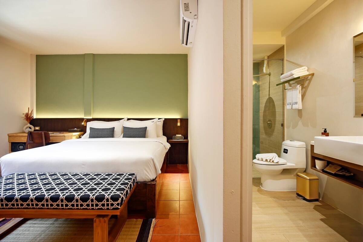 Een hotelkamer met een bed, nachtkastje, lamp en uitzicht op de badkamer.