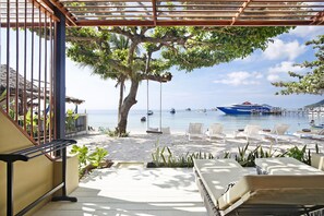 Un patio frente a la playa con sillones, una hamaca y vista al mar y barcos.